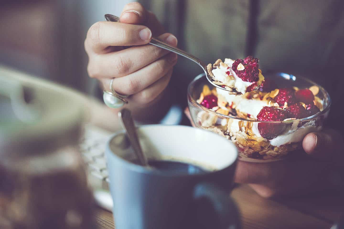 A bowl of yogurt, granola, and berries, with a cup of coffee