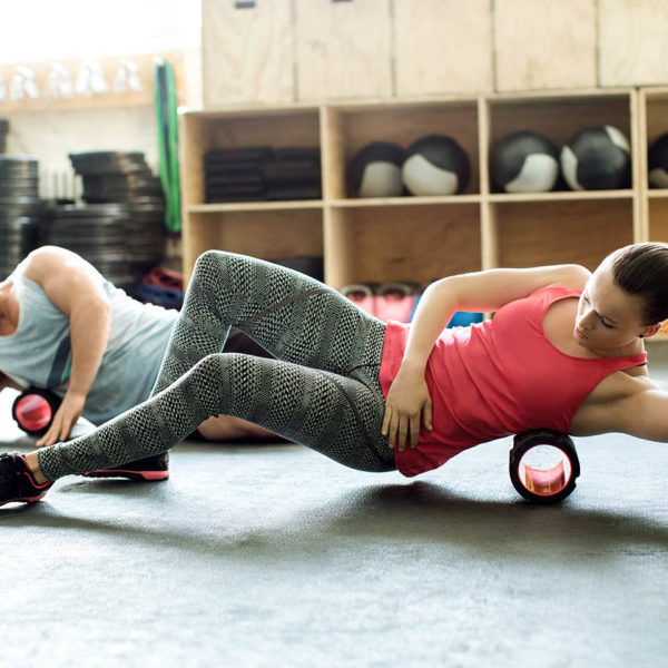 A woman and man using foam rollers in the gym