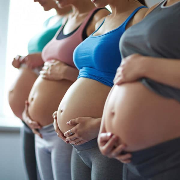 Four pregnant women in workout clothes, holding their bellies