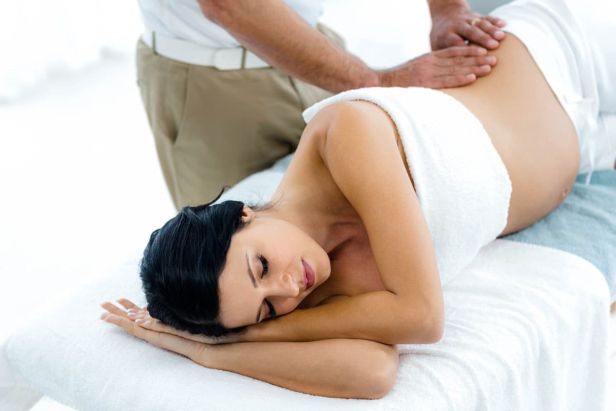 A pregnant woman lying on her side, and receiving a massage.