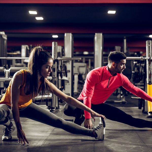 A man and woman doing stretches in a gym.