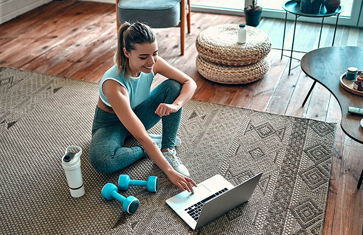 Woman setting up a workout on a laptop, in her living room.